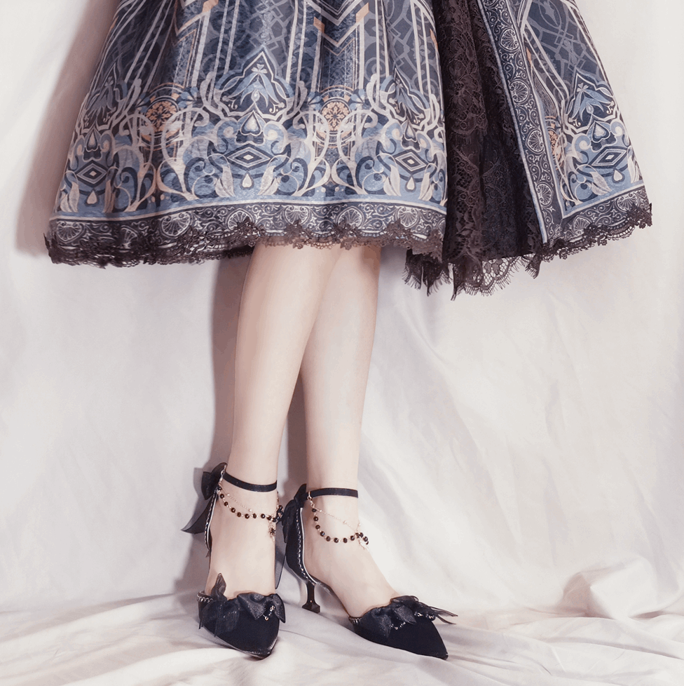 Person wearing a patterned dress and black shoes with decorative straps on a white background