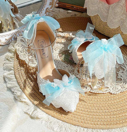 Pair of white high-heeled shoes with blue ribbons on a decorative surface.