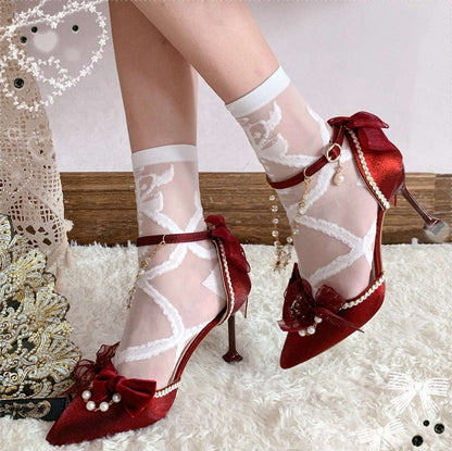 Red high-heeled shoes with lace and bow details on a textured surface.