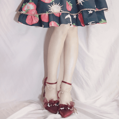 Close-up of a person wearing a floral dress, white stockings, and red shoes with decorative bows on a light background.