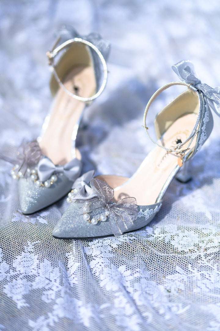 Pair of silver high-heeled shoes with decorative ribbons on a textured fabric background
