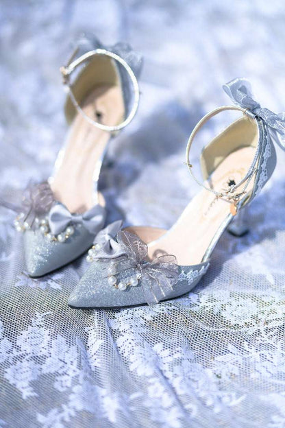 Pair of silver high-heeled shoes with decorative ribbons on a textured fabric background