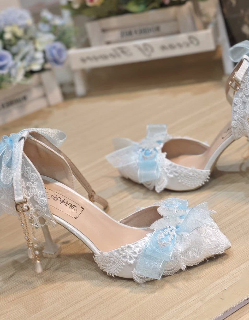 White lace high-heeled shoes with blue floral decorations on a wooden surface.