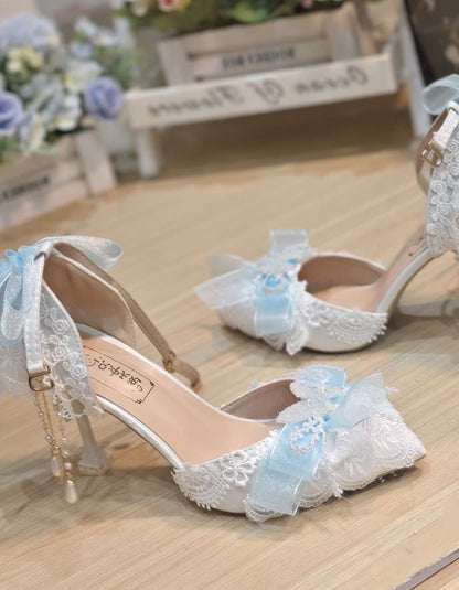 White lace high-heeled shoes with blue floral decorations on a wooden surface.