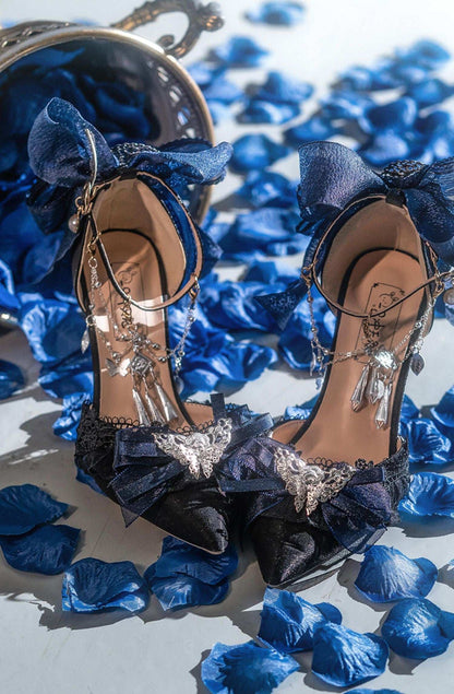 Navy high-heeled shoes with decorative bows on a bed of blue petals.