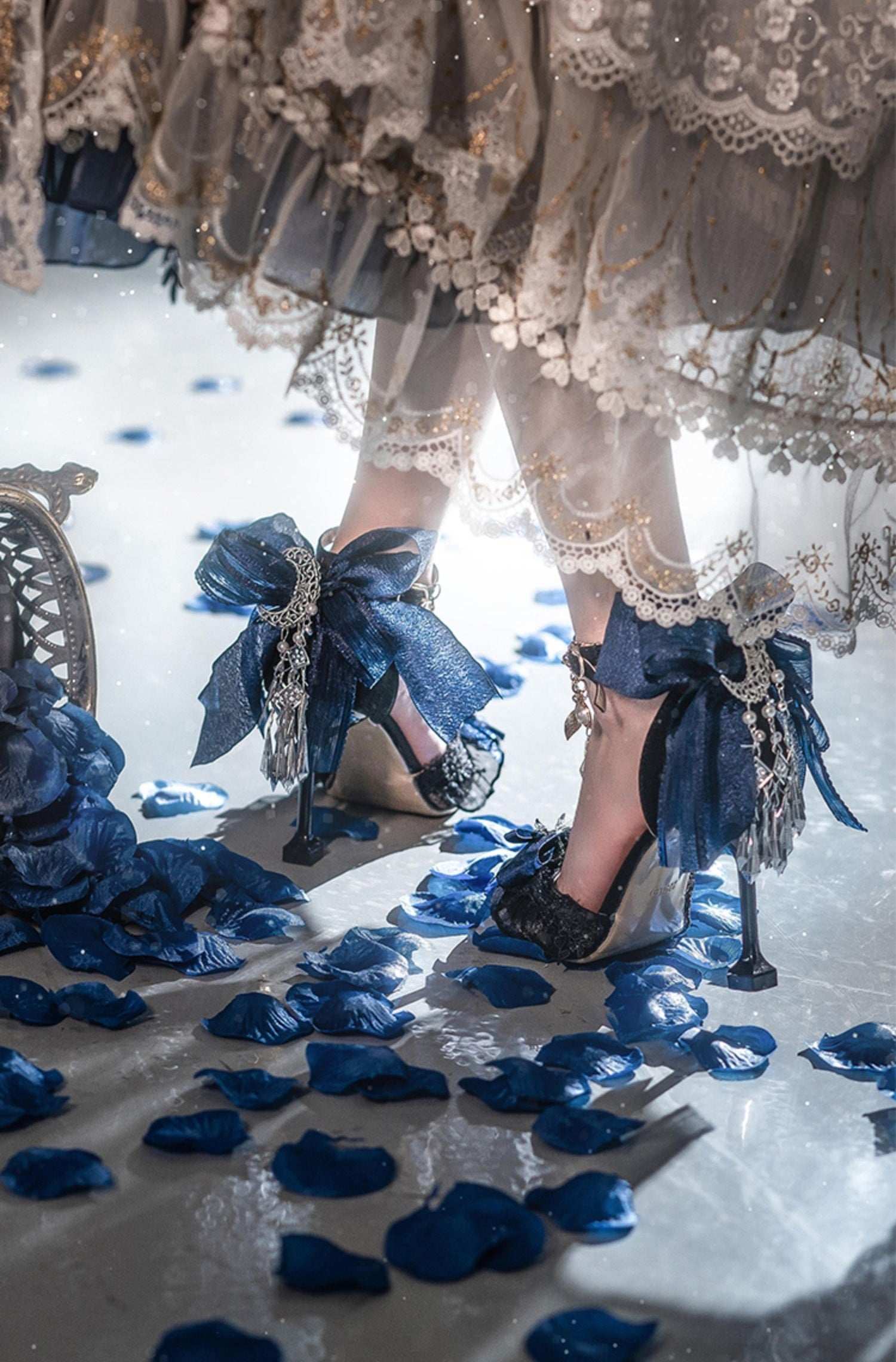 High-heeled shoes with decorative bows on a reflective surface with blue petals.