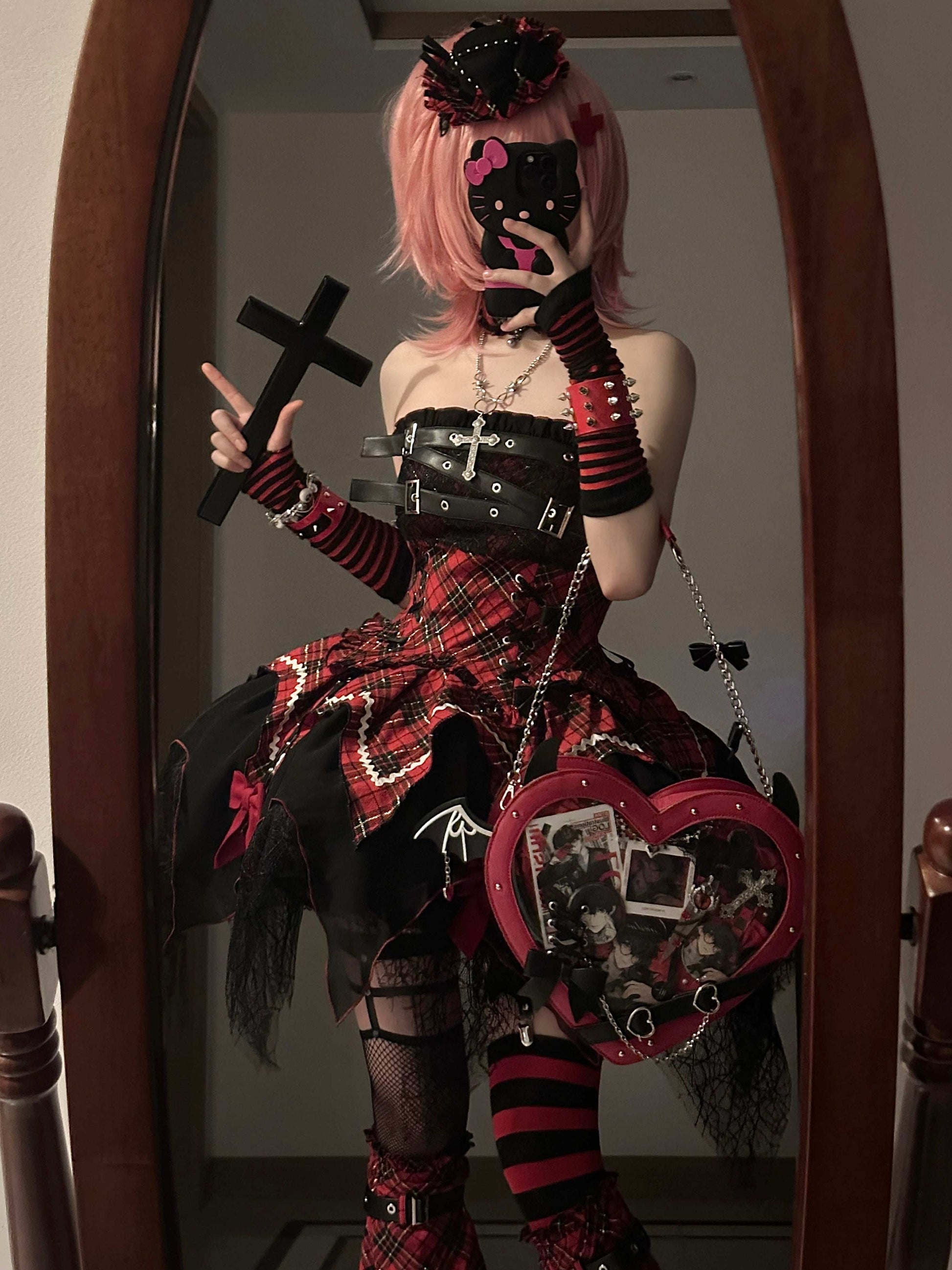 Person in a detailed and colorful outfit with a cross, mask, and heart-shaped bag in front of a mirror.