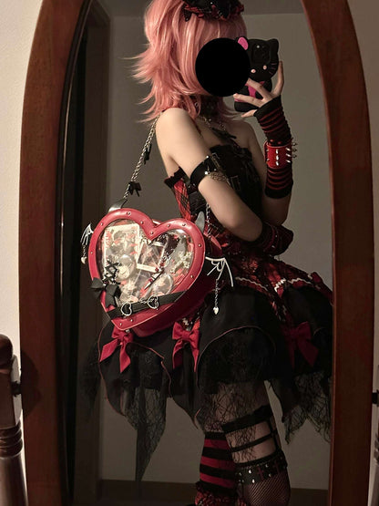 Person with pink hair holding a black cat, wearing a black and red outfit with a heart-shaped bag.