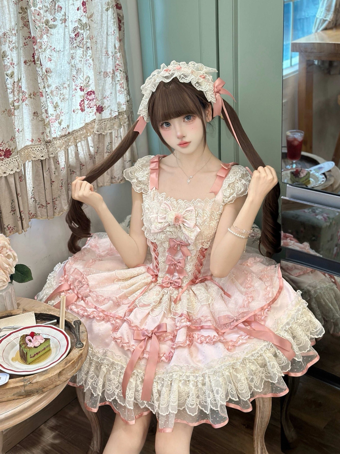 Person wearing a pink and white Lolita-style dress sitting in a room with floral curtains.