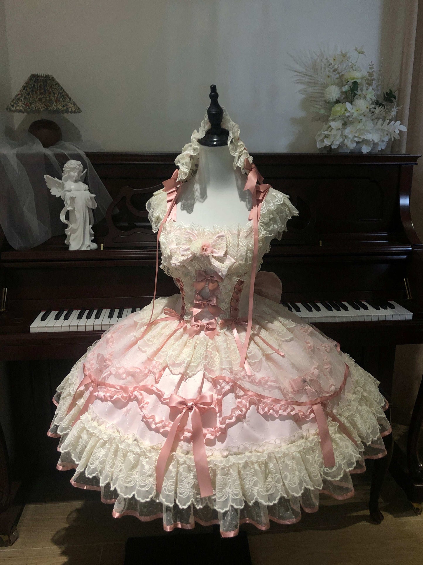 Delicate pink lace dress on a mannequin in front of a piano