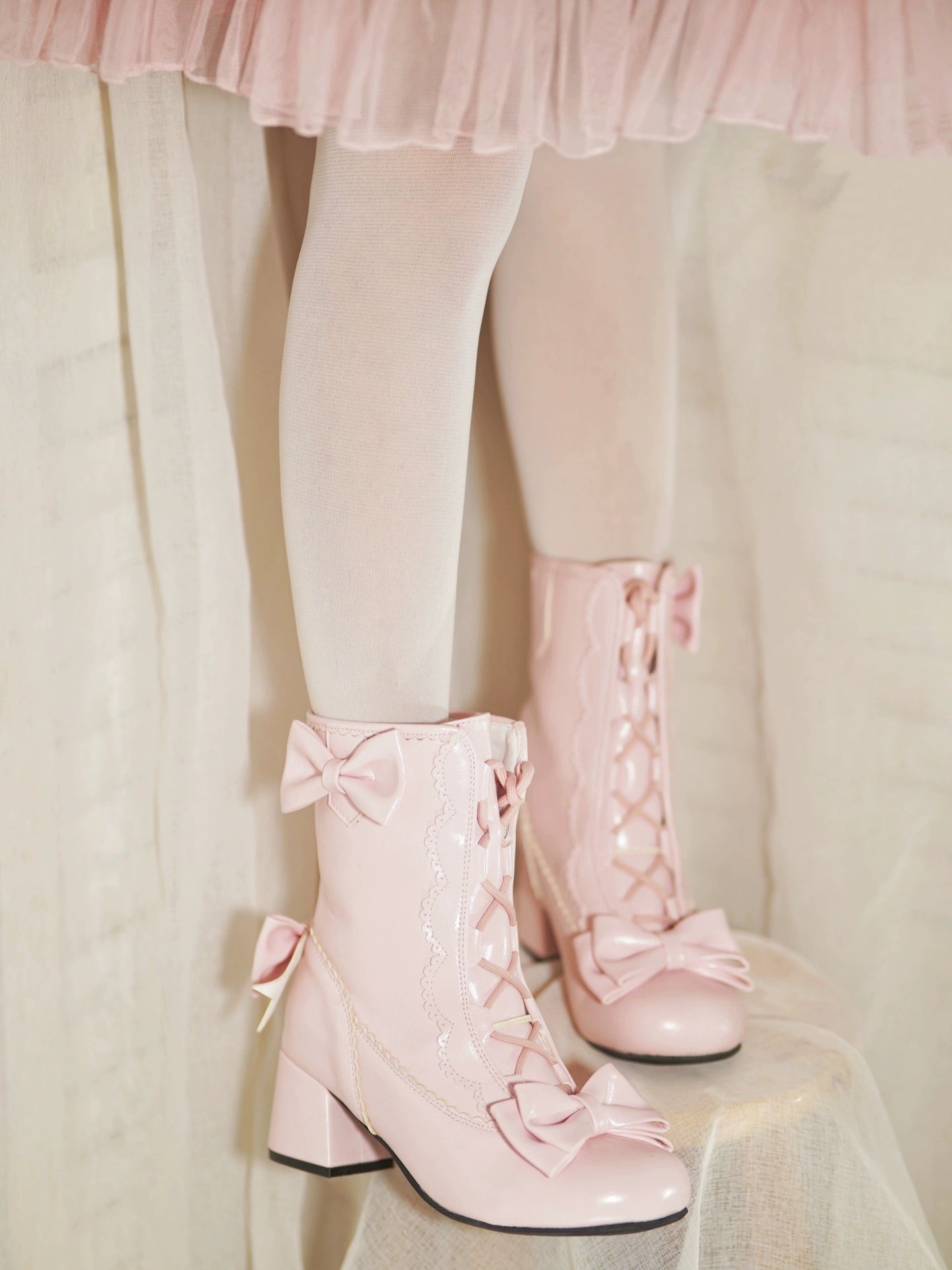 Pink lace-up boots with bows worn with sheer white stockings against a light background