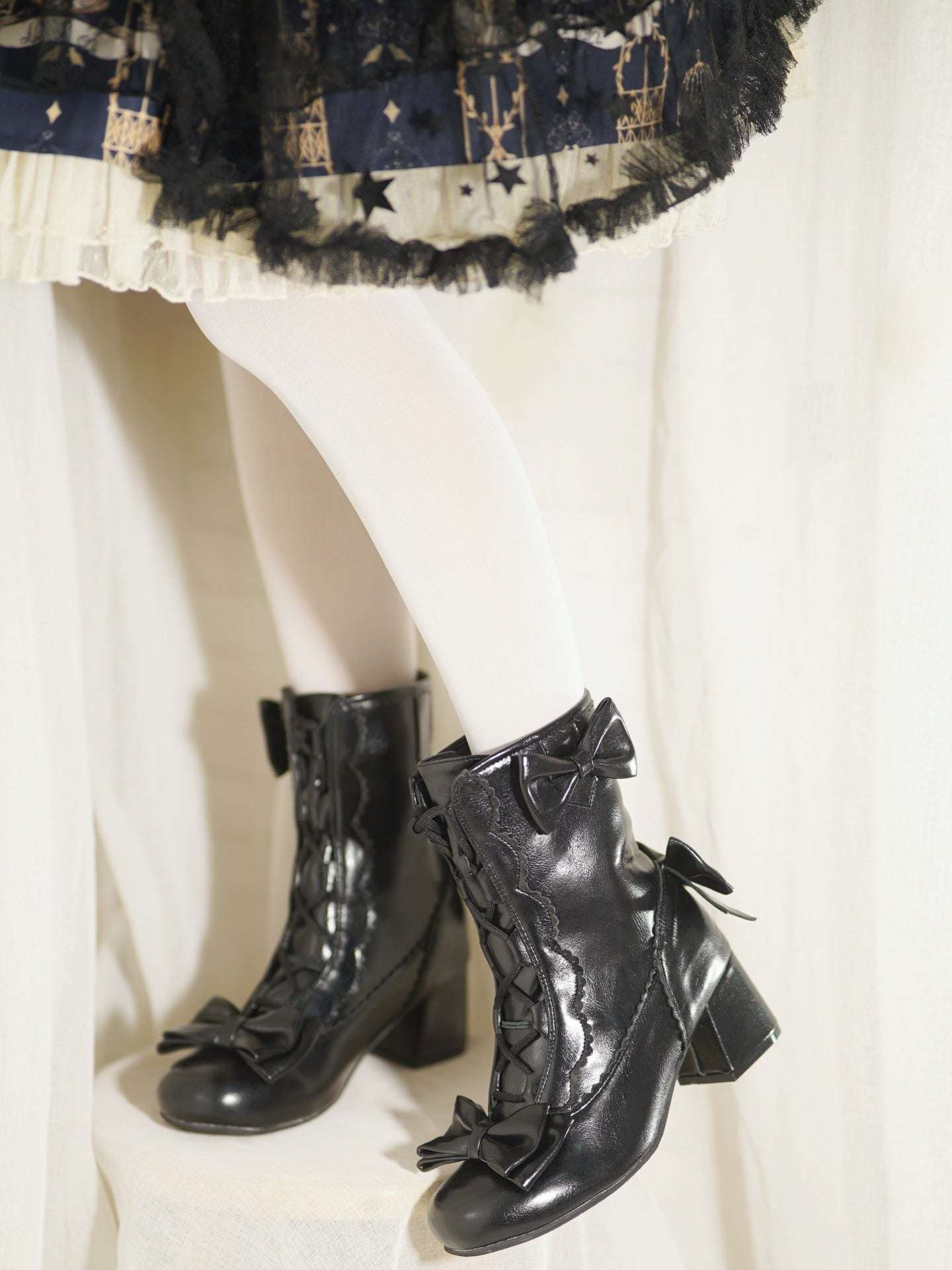 Black lace-up boots with bows worn with a plaid skirt on a white background
