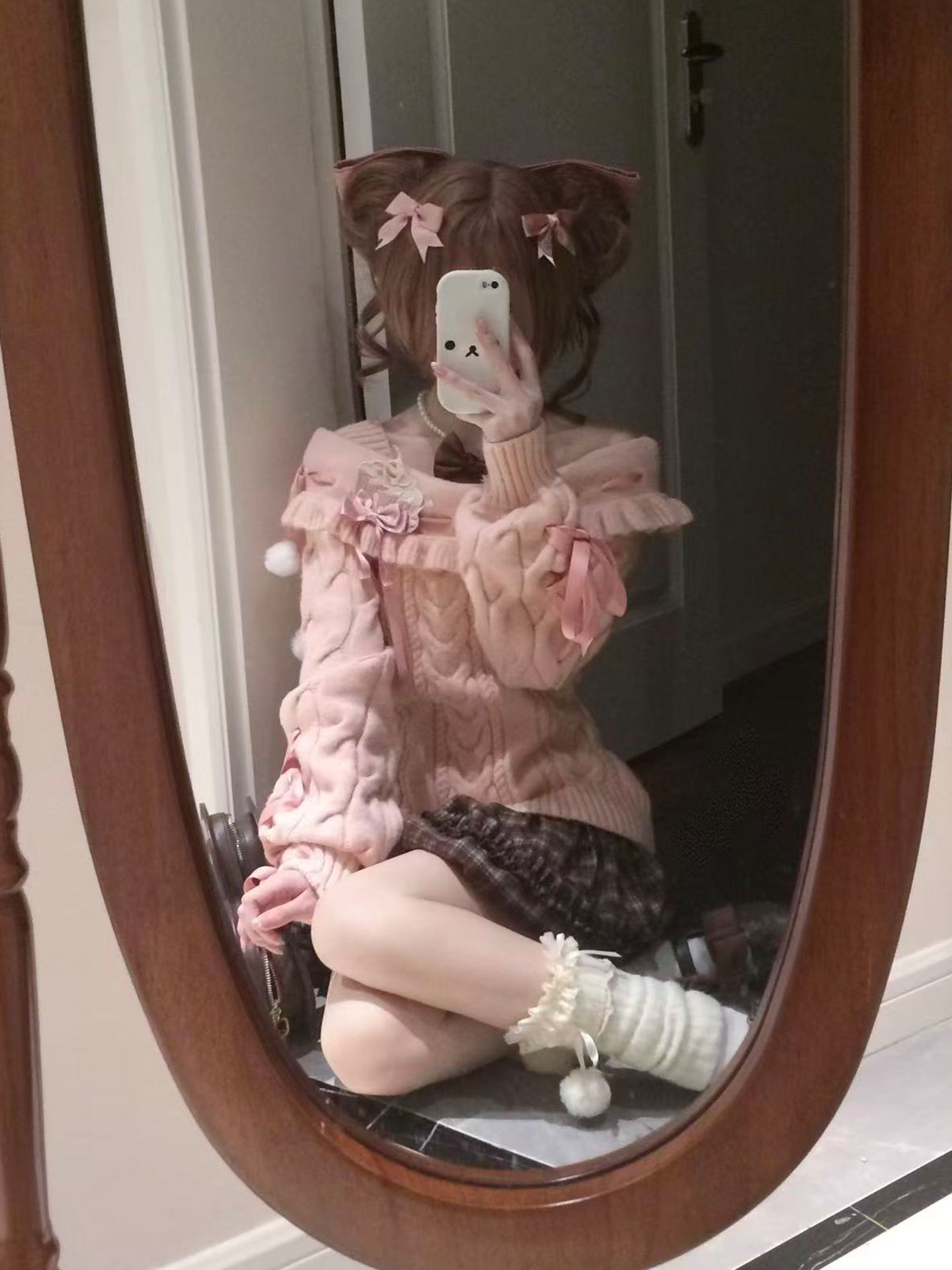 Person wearing a pink outfit with ruffles and a brown hat sitting in front of a mirror.