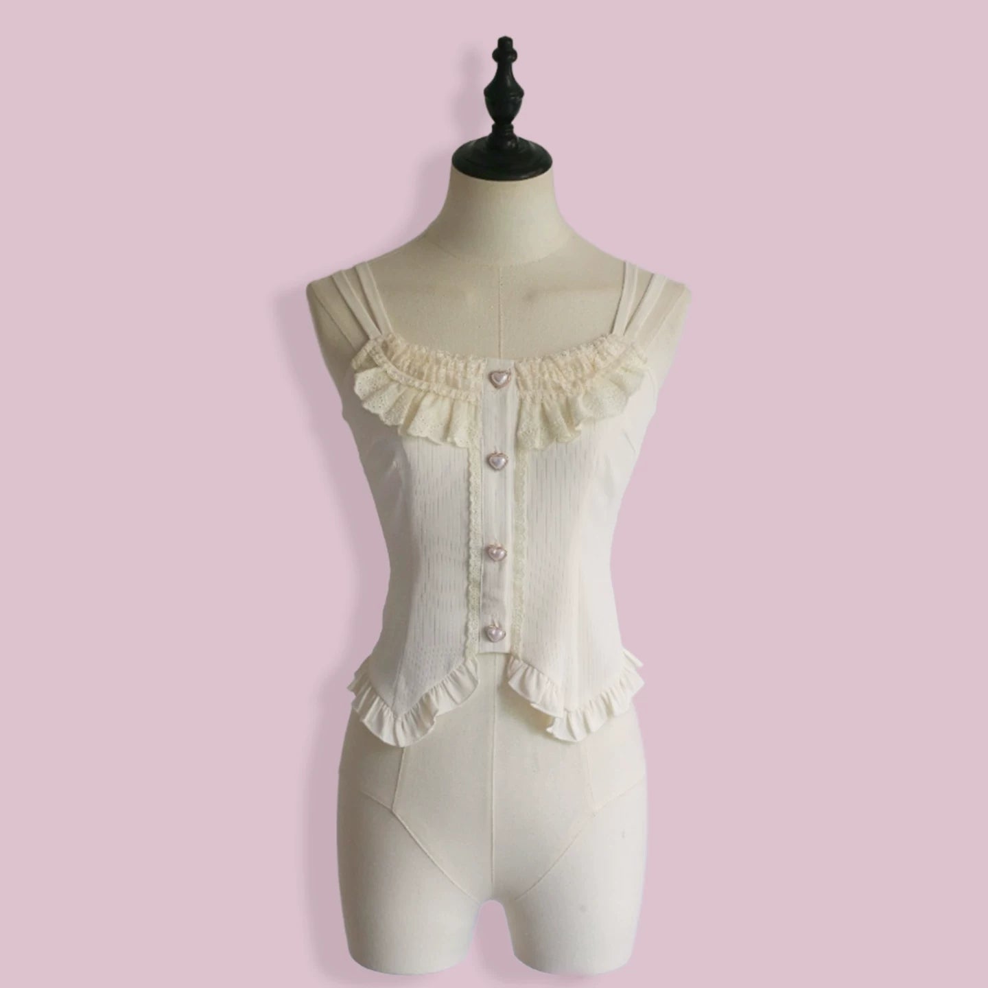 White camisole with ruffled details on a mannequin against a pink background