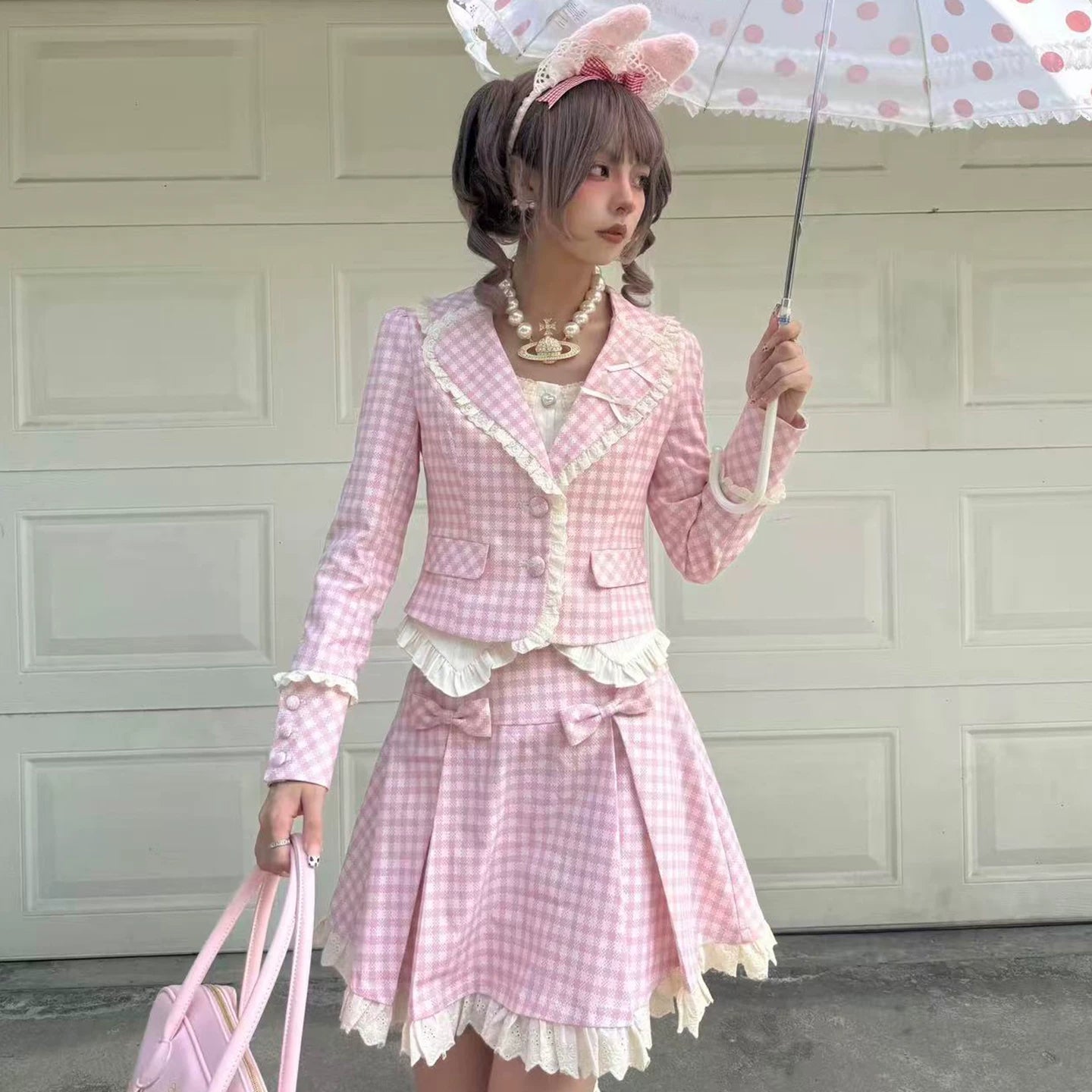 Person wearing a pink checkered outfit with a polka dot umbrella in front of a garage door.