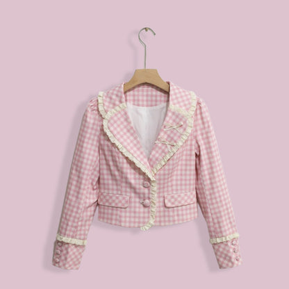 Pink checkered jacket with ruffled trim on a hanger against a pink background