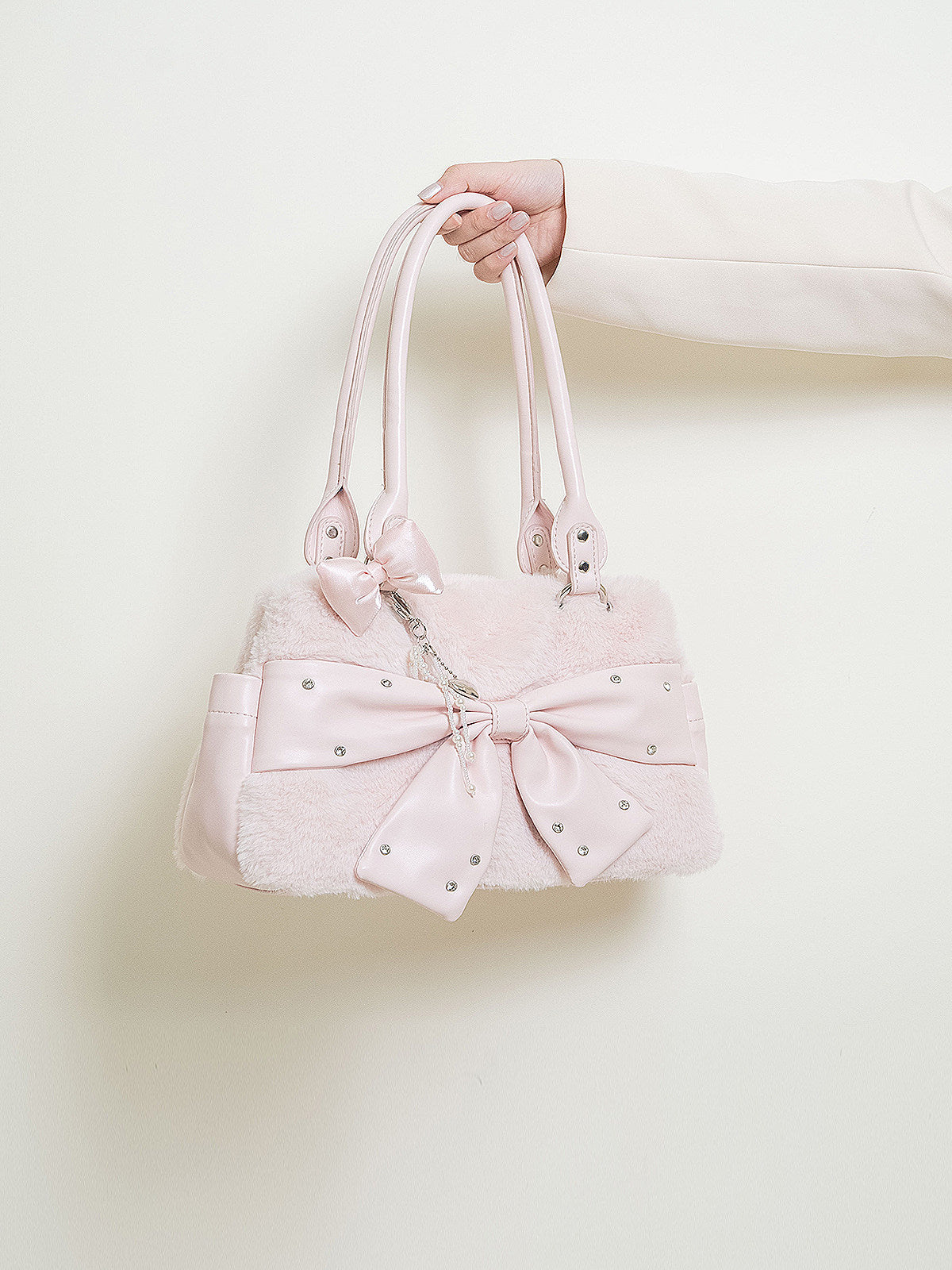 Pink handbag with a large bow held by a hand against a light background