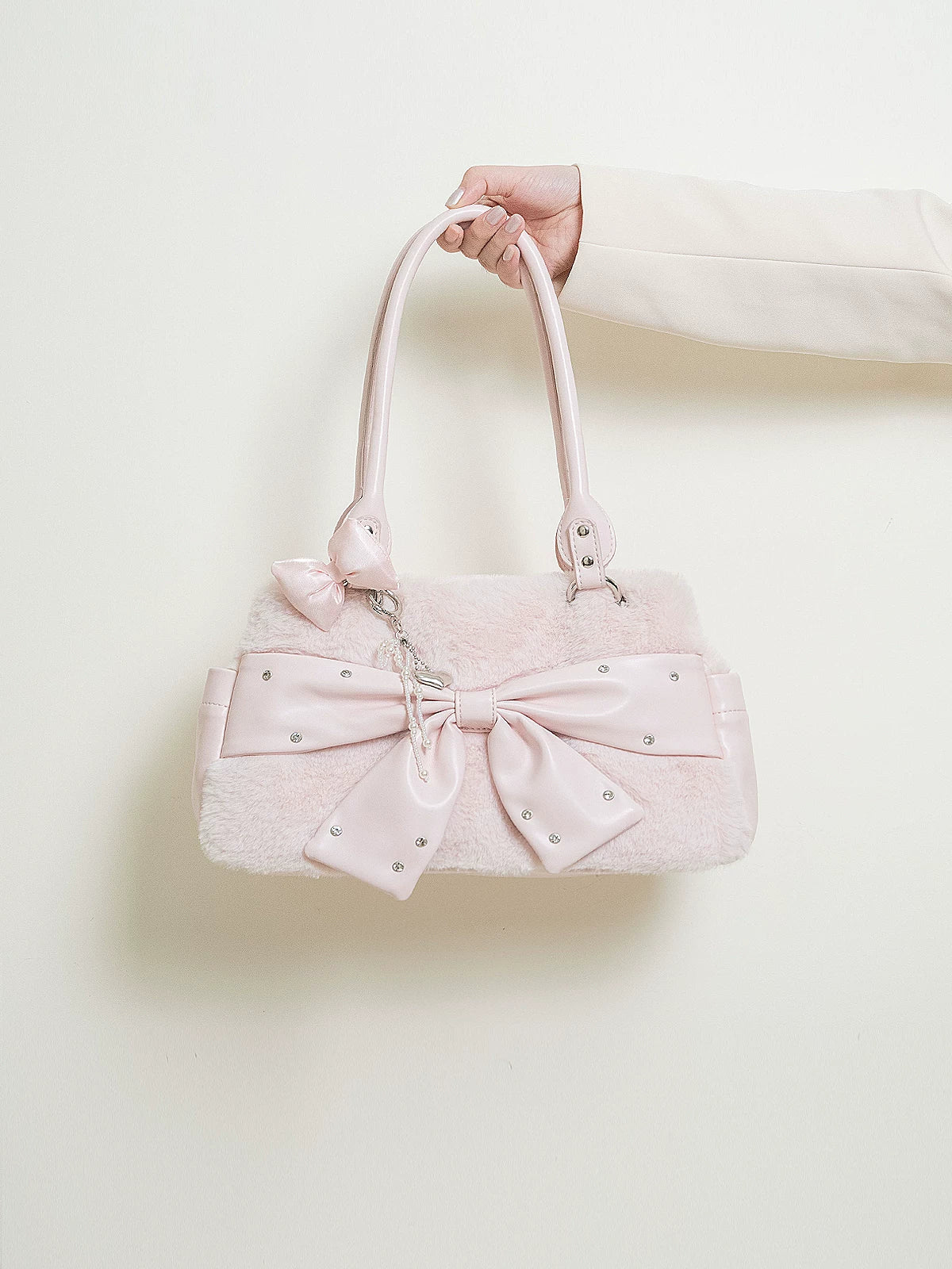Pink handbag with a bow held by a hand against a light background