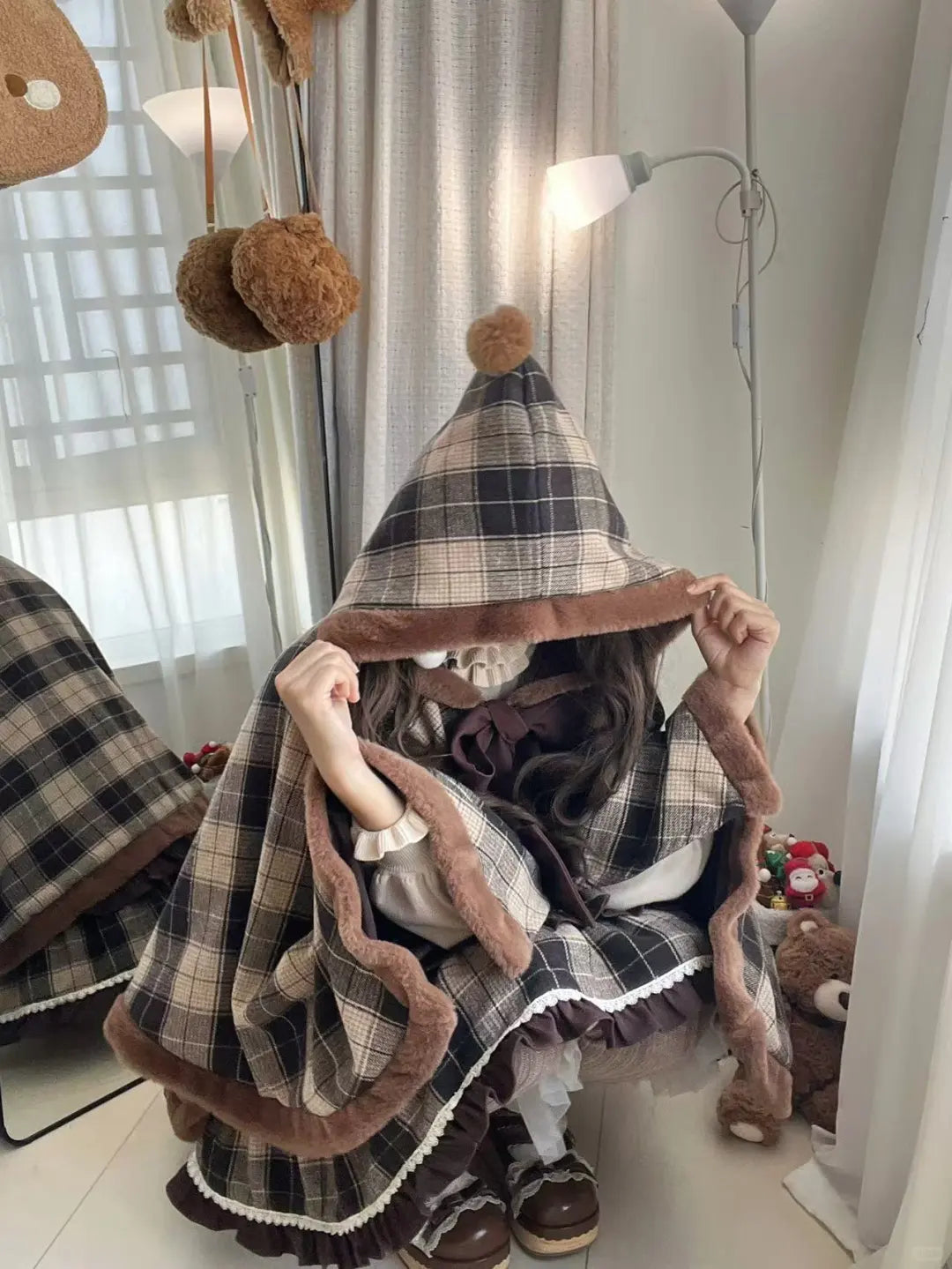 A girl in a plaid outfit with brown trim, sitting on a white floor.