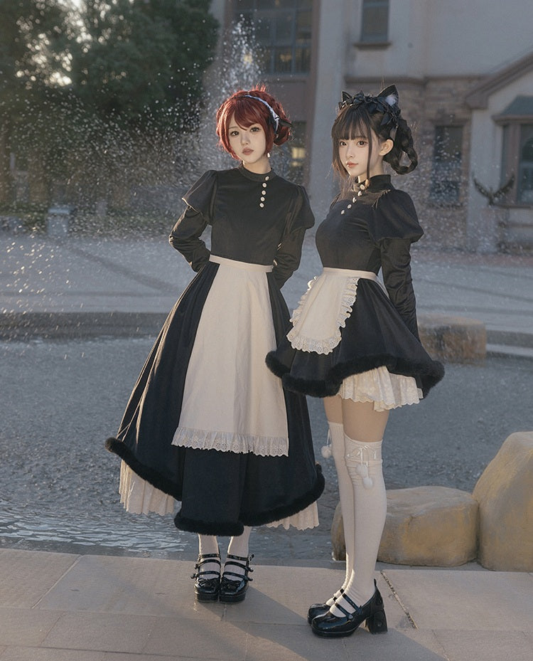 Two women in lolita black and white maid outfits standing outdoors near a fountain.