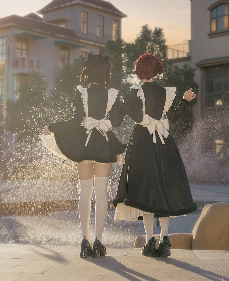 Two people in lolita black dresses with white aprons standing in front of a fountain.
