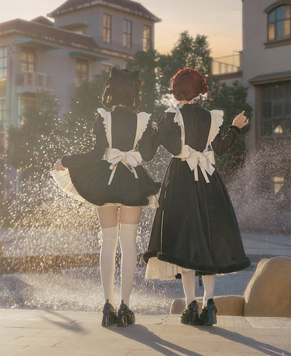 Two people in lolita black dresses with white aprons standing in front of a fountain.