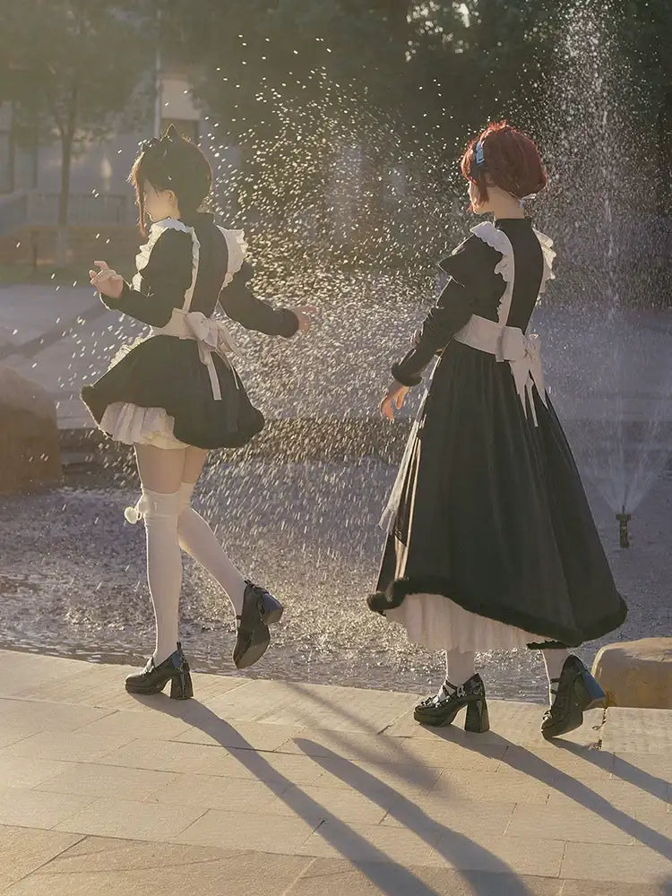 Two women in lolita black dresses with white aprons standing near a fountain.