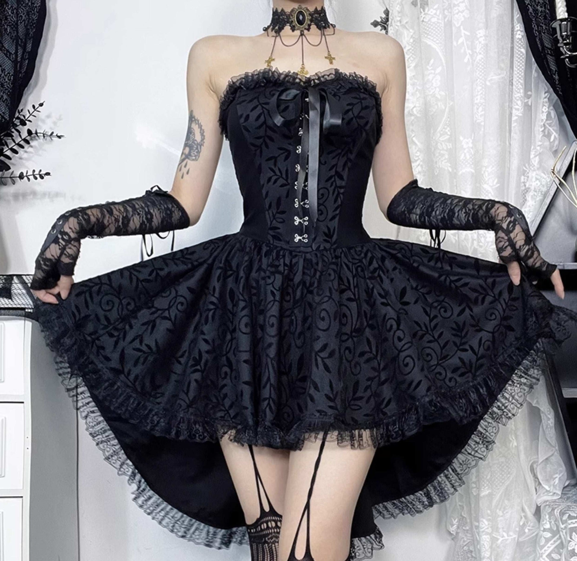 Person wearing a black lace dress with long gloves against a white curtain background