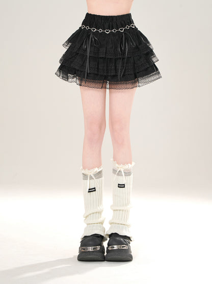 Person wearing a black tiered skirt with silver chain detail, white knee-high socks, and black shoes on a light background.