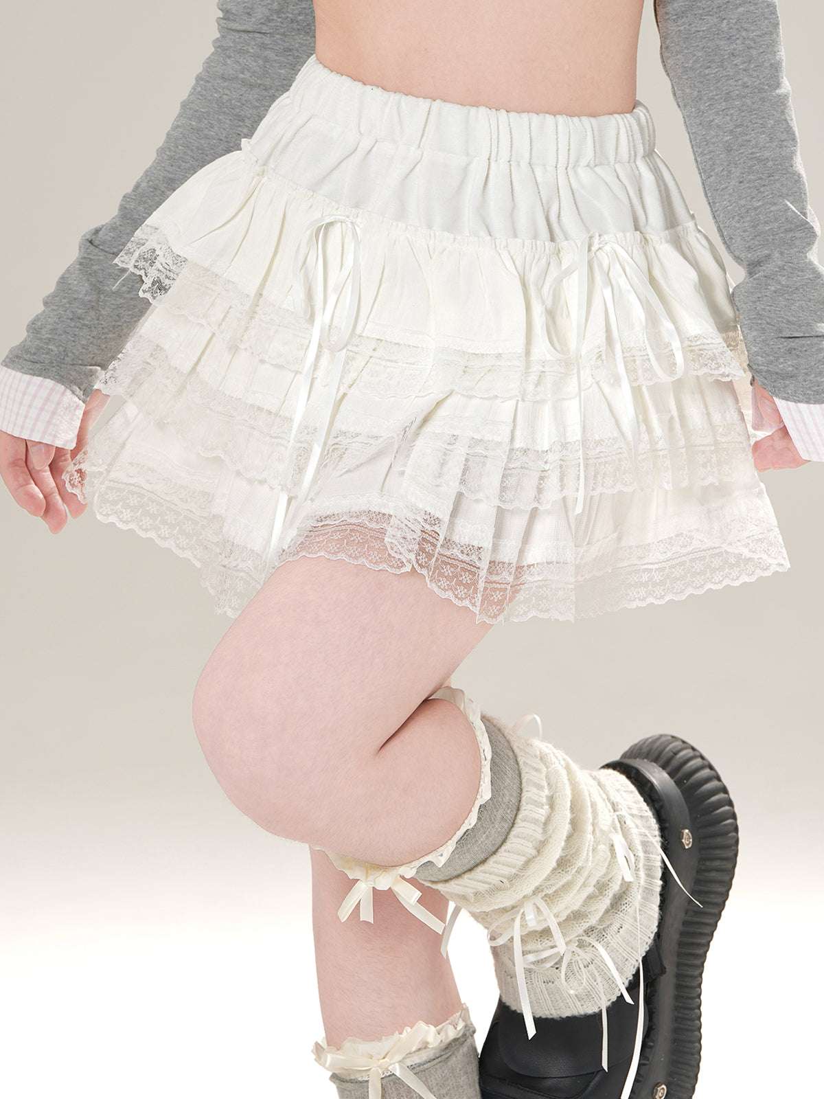 Person wearing a white lace skirt and gray leg warmers on a plain background