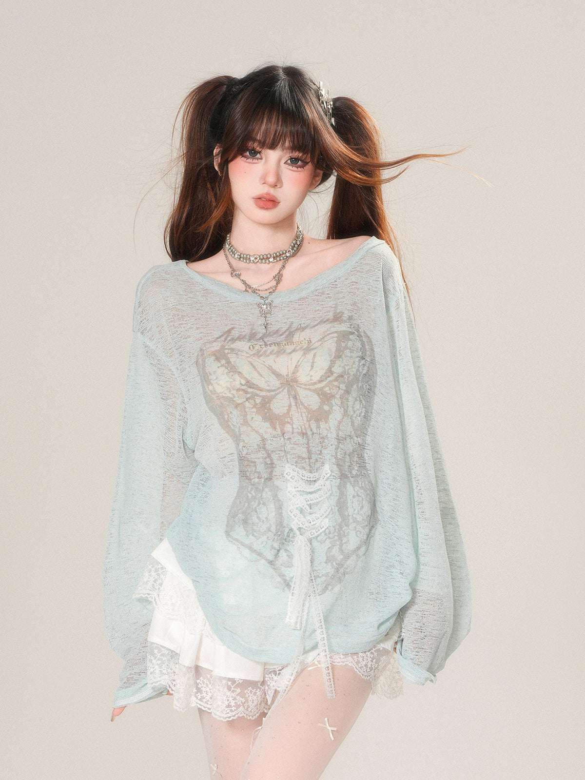 Woman wearing a light blue sheer top with lace details on a plain background