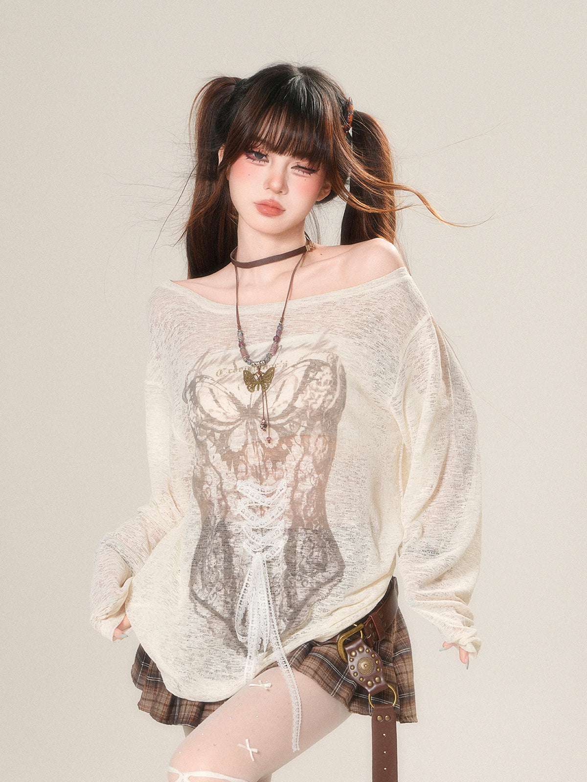 Person wearing a sheer top with lace details and plaid skirt on a plain background