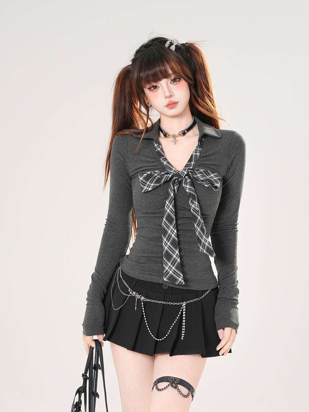 Woman wearing a dark gray long-sleeve shirt with plaid accents and a black pleated skirt on a white background.