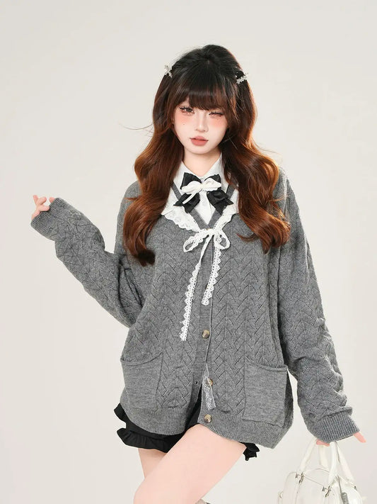 Woman wearing a gray cardigan with a white lace top against a plain background