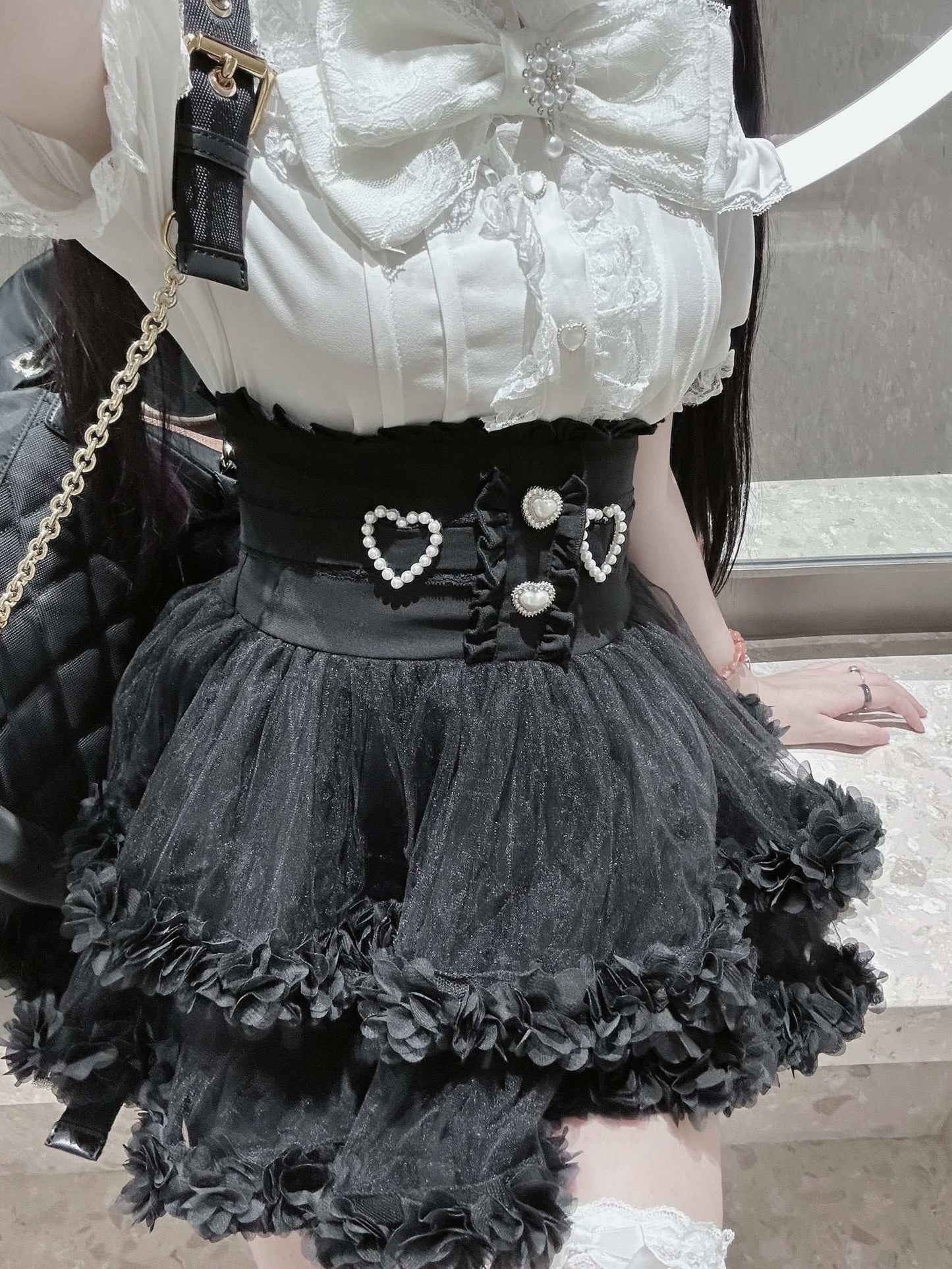 Person wearing a white lace top and black ruffled skirt with heart details.